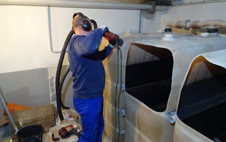 Person mit Gehörschutz arbeitet mit einer Maschine um eine alte Batterietankanlage auszubauen
